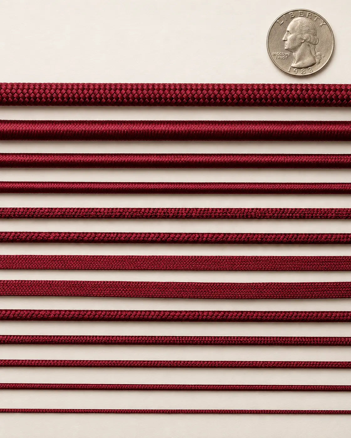 Thirteen burgundy cord types arranged in horizontal rows beside a US quarter for relative scale